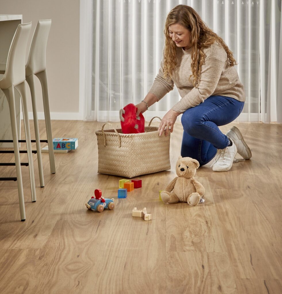 Woman tidying toys on light wood-look flooring